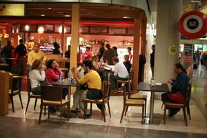 airport, artificial lighting, autumn, cafe, evening, eye level view, furniture, group, indoor lighting, interior, Madrid, people, sitting, Spain